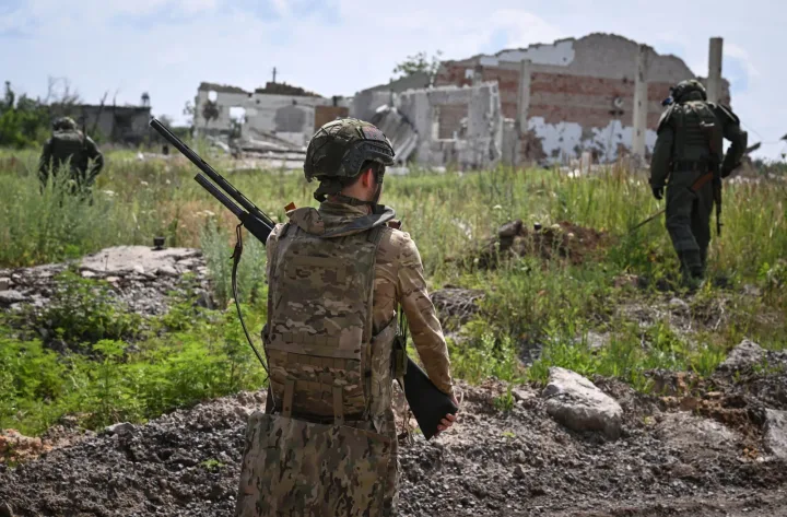 Soldați ruși în zonă de conflict, clădiri distruse în fundal.