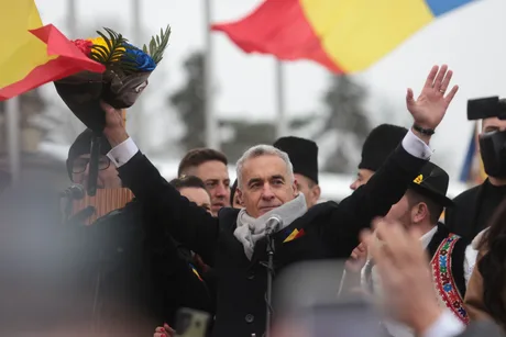 Călin Georgescu salută mulțimea cu un buchet de flori în mână.