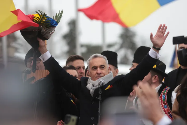 Călin Georgescu salută mulțimea cu un buchet de flori în mână.