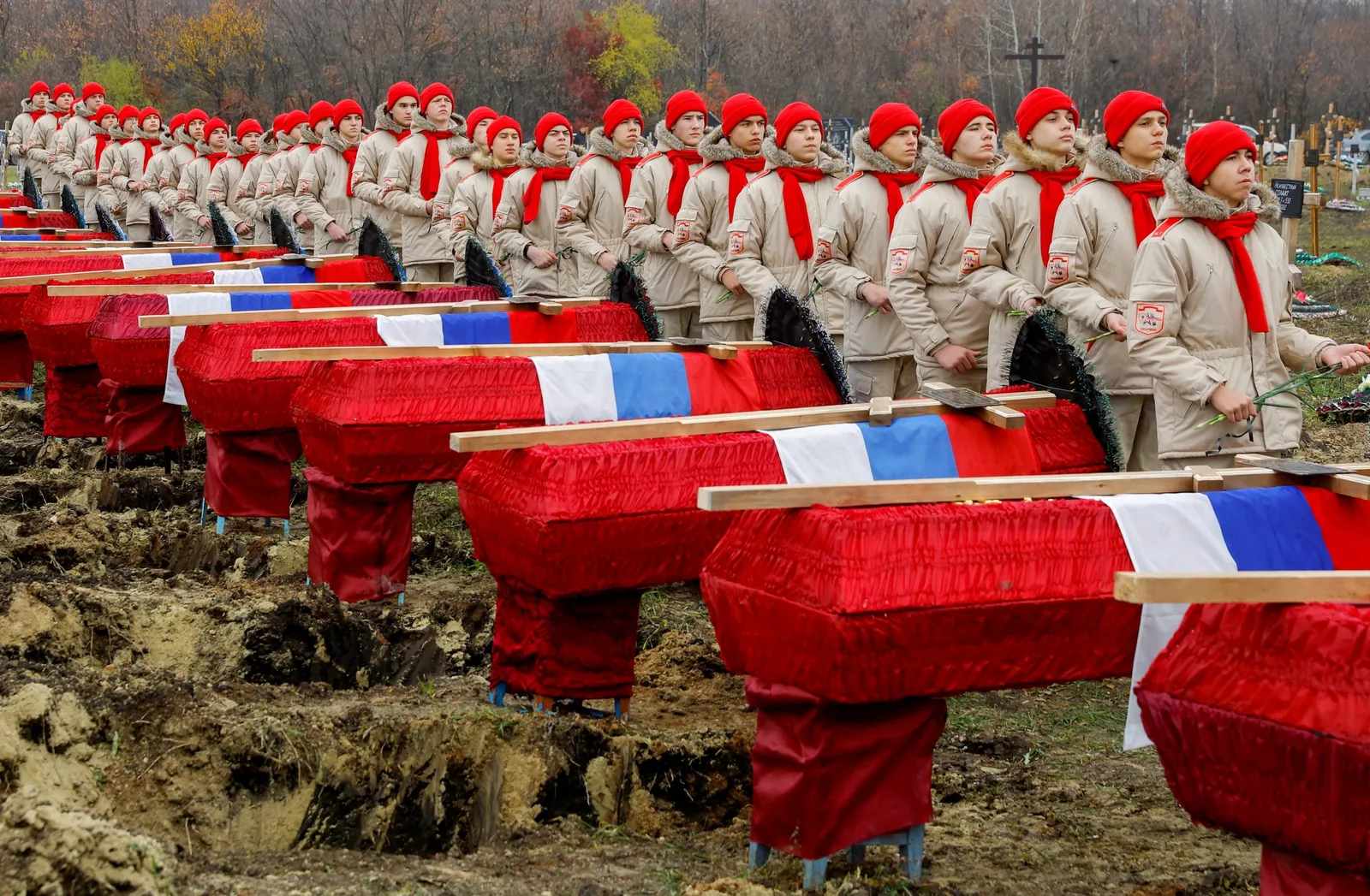 Rând de sicrie roșii într-un cimitir, simbolizând pierderile umane.