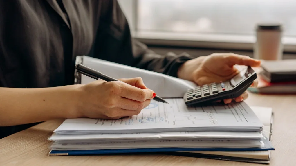 Persoană care completează documente financiare cu un calculator.