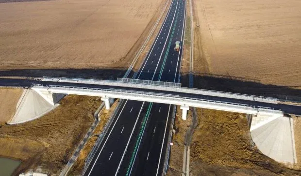 Drum expres cu bandă de urgență, lucrări în desfășurare și peisaj rural.