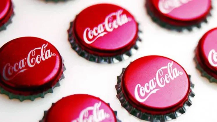Capace de sticlă Coca-Cola aranjate pe o masă albă.