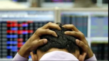 Un investitor îngrijorat în fața ecranelor bursiere aglomerate.