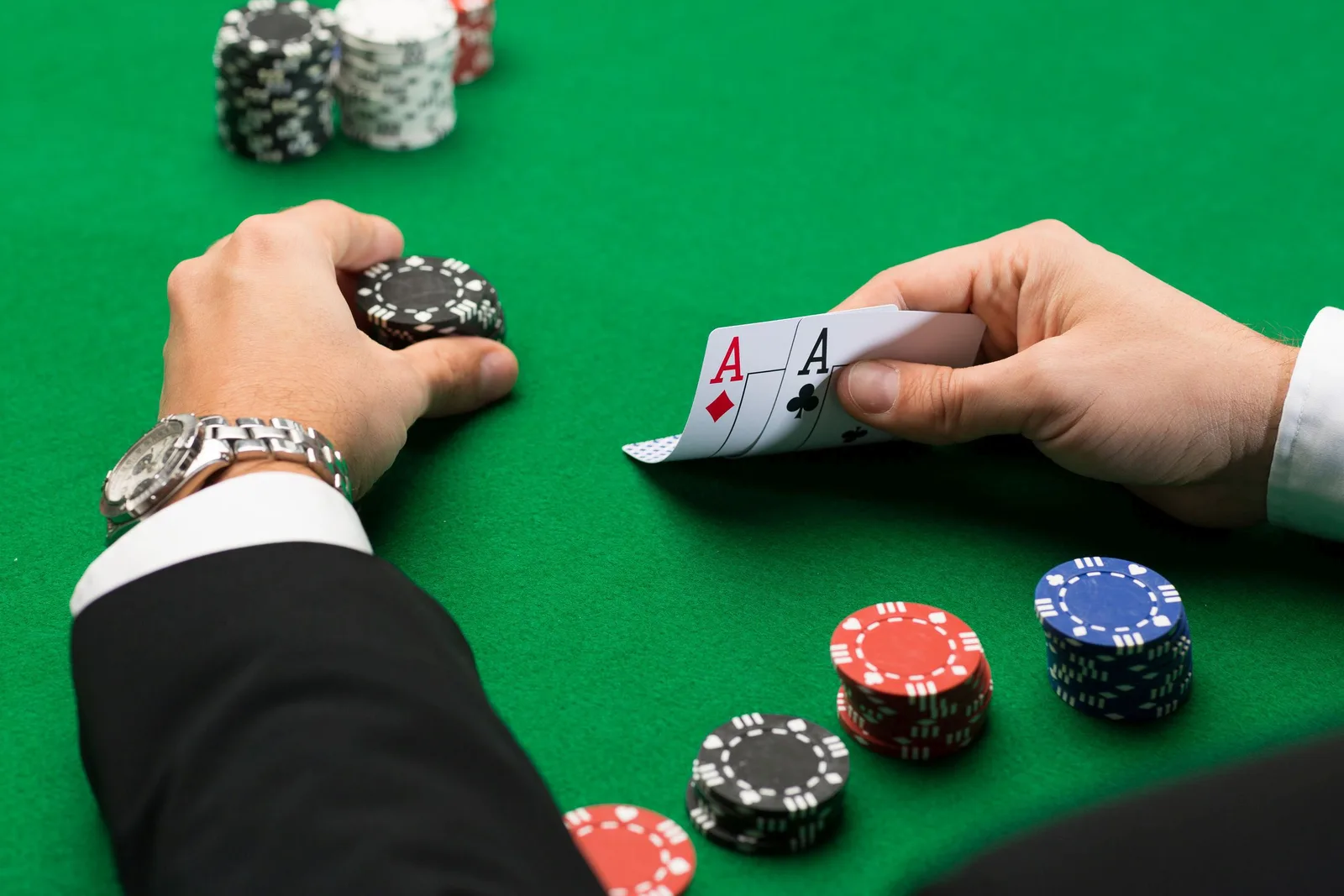 Persoană jucând cărți la o masă de poker, cu fise colorate în jur.