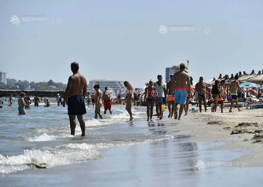 Plajă aglomerată pe litoralul românesc, cu turiști la apă și soare.