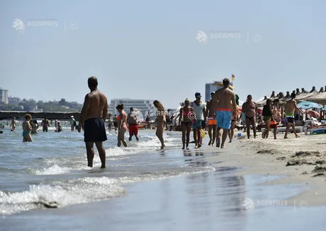 Plajă aglomerată pe litoralul românesc, cu turiști la apă și soare.