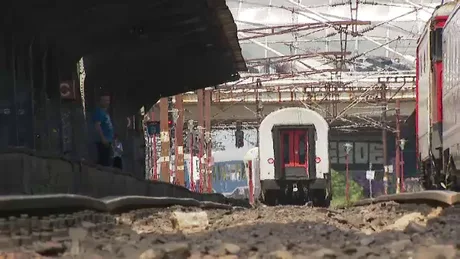 Gara feroviară cu trenuri parcate și călători așteptând.