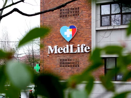 Logo-ul MedLife pe un zid de cărămidă, înconjurat de plante verzi.