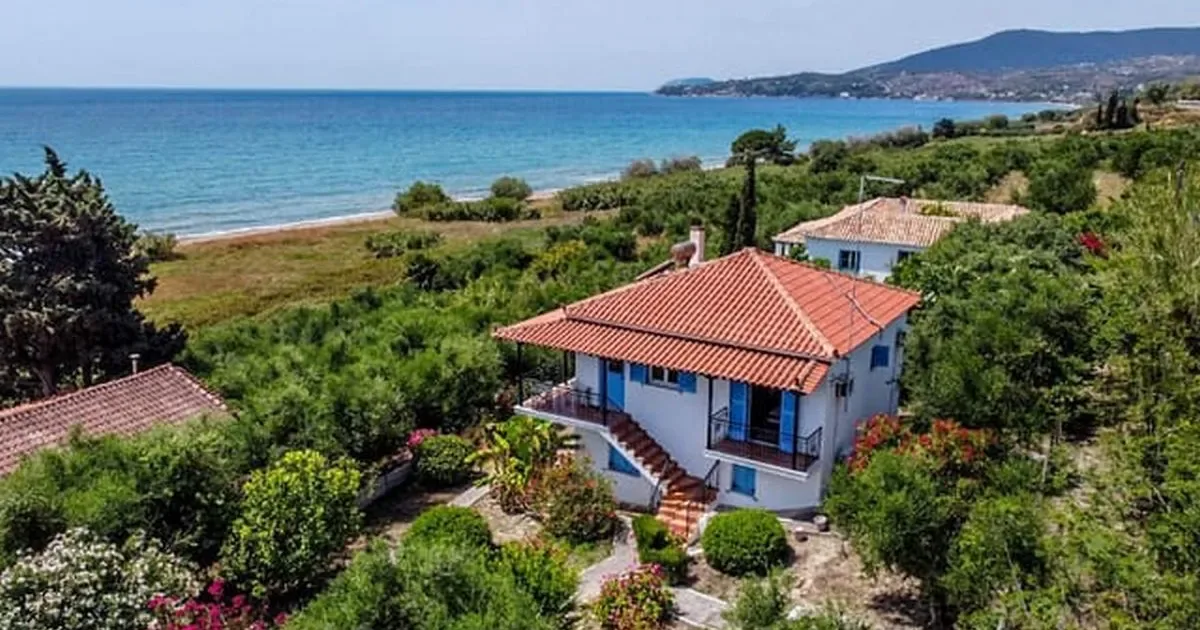 O locuință pe malul mării în Grecia, înconjurată de vegetație luxuriantă.