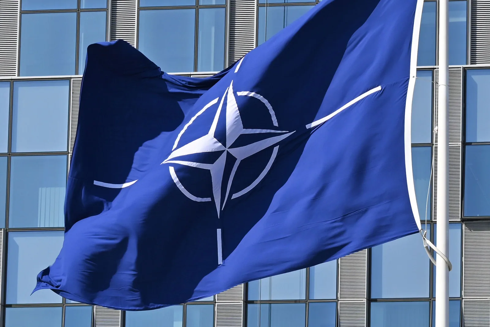 Steagul NATO fluturând în fața unei clădiri moderne.