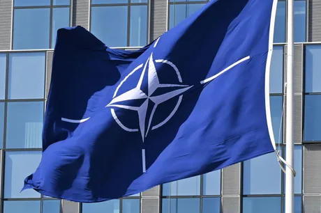 Steagul NATO fluturând în fața unei clădiri moderne.