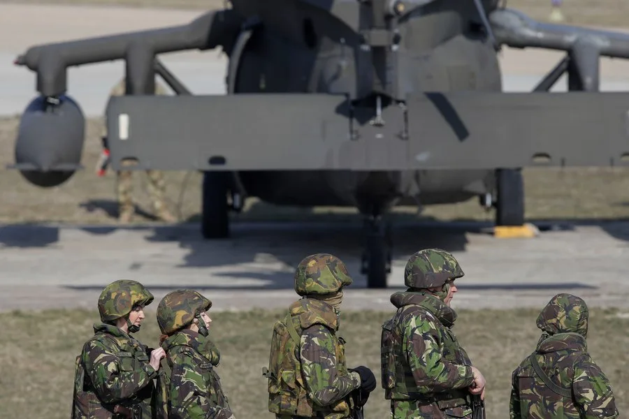 Soldați în uniformă militară lângă un elicopter pe un teren de antrenament.