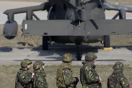 Soldați în uniformă militară lângă un elicopter pe un teren de antrenament.
