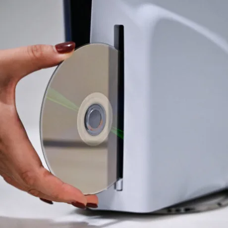 O persoană introduce un disc într-o consolă de jocuri.