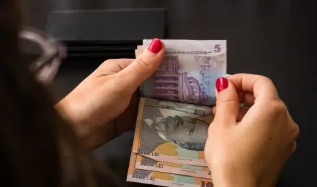 Mână numărând bancnote românești pe un fundal întunecat.