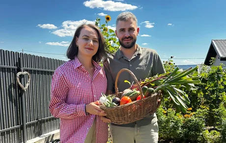 Cuplu fericit ținând o ladă cu legume proaspete în grădina lor.