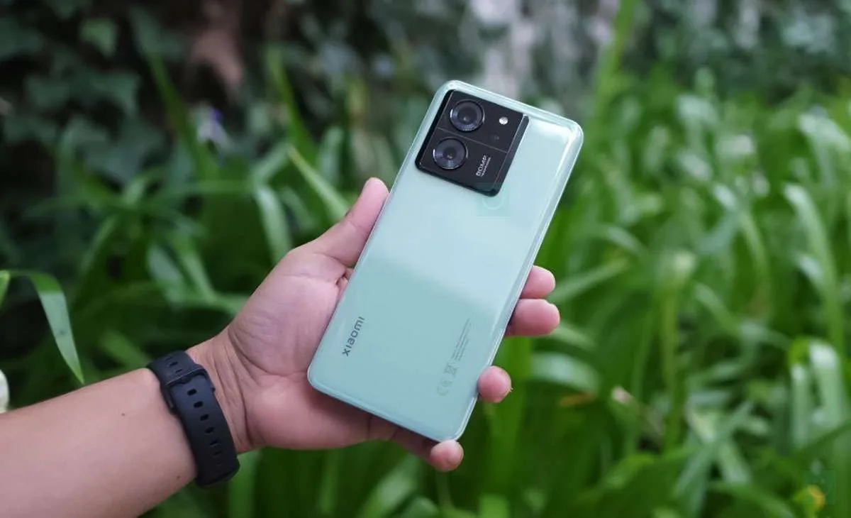 Un telefon Xiaomi 13T verde, ținut în mână, pe fundal de plante verzi.