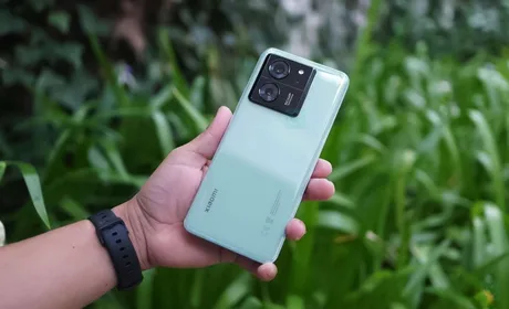 Un telefon Xiaomi 13T verde, ținut în mână, pe fundal de plante verzi.