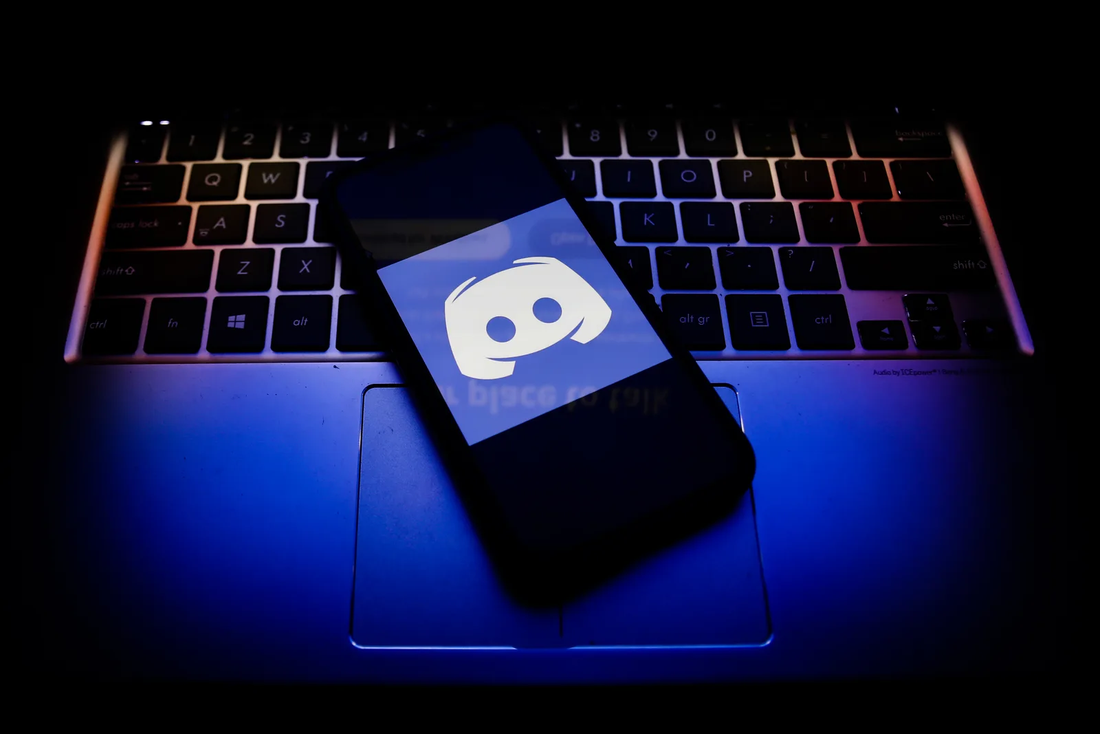 Logo-ul Discord pe un laptop, iluminat de un fundal întunecat.