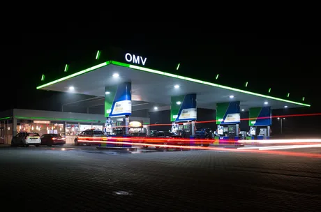 Stație de carburanți OMV iluminată noaptea, cu mașini la pompă.