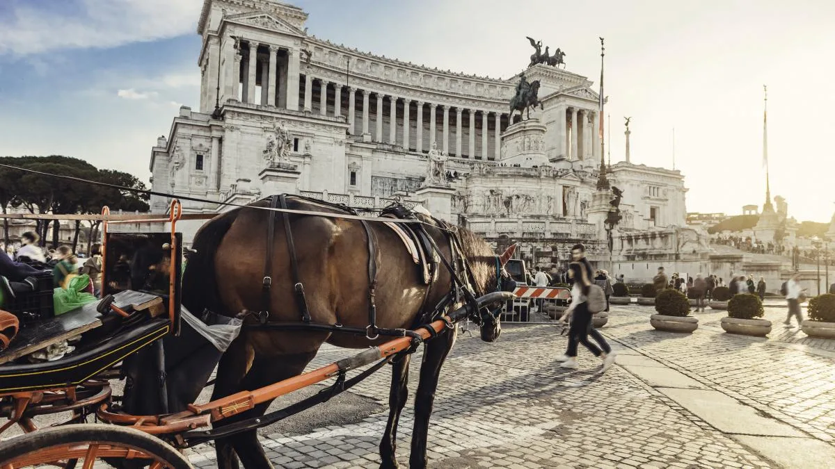 Trăsură turistică trasă de cai în fața unui monument din Roma.