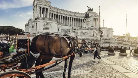 Trăsură turistică trasă de cai în fața unui monument din Roma.