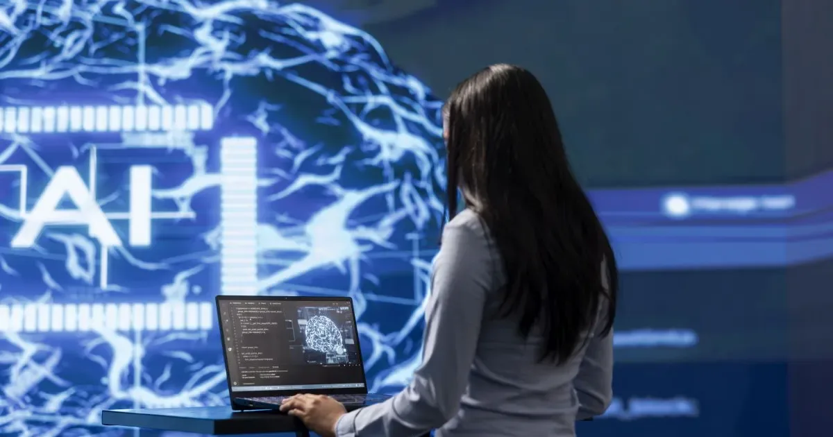 O persoană lucrează la un laptop, în fața unui panou cu teme de inteligență artificială.