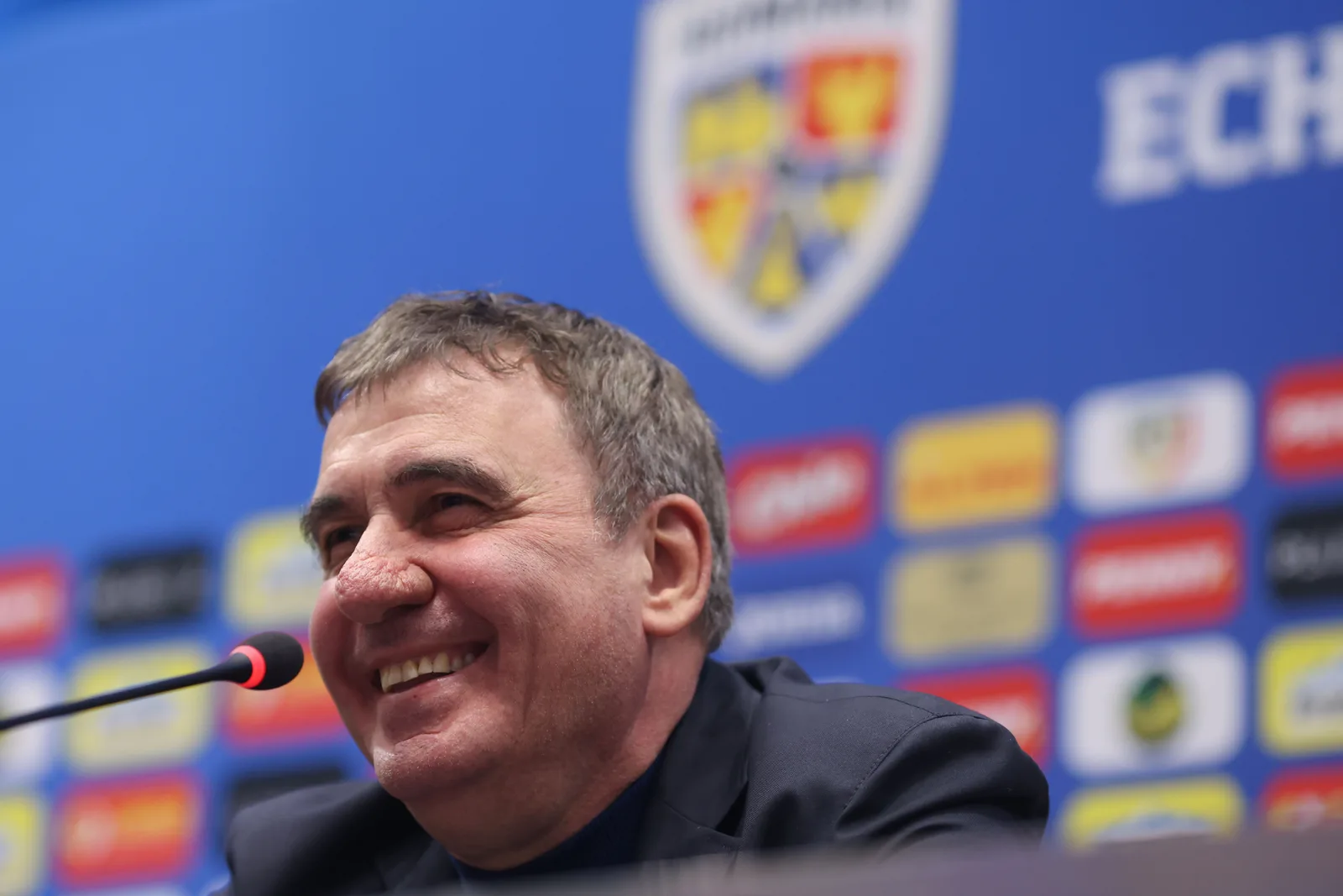 Gică Hagi zâmbind în timpul unei conferințe de presă despre naționala României.