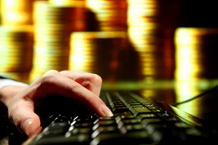 O mână pe o tastatură, în fundal monede strălucitoare.