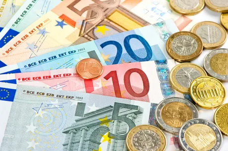 Bancnote și monede euro aranjate pe o suprafață albă.