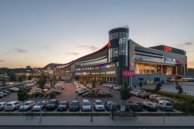 Centrul comercial Ozas din Vilnius, iluminat la apus, cu parcarea plină.