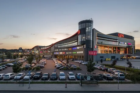 Centrul comercial Ozas din Vilnius, iluminat la apus, cu parcarea plină.