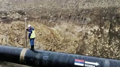 Un muncitor inspectează un conductă de petrol în teren accidentat.