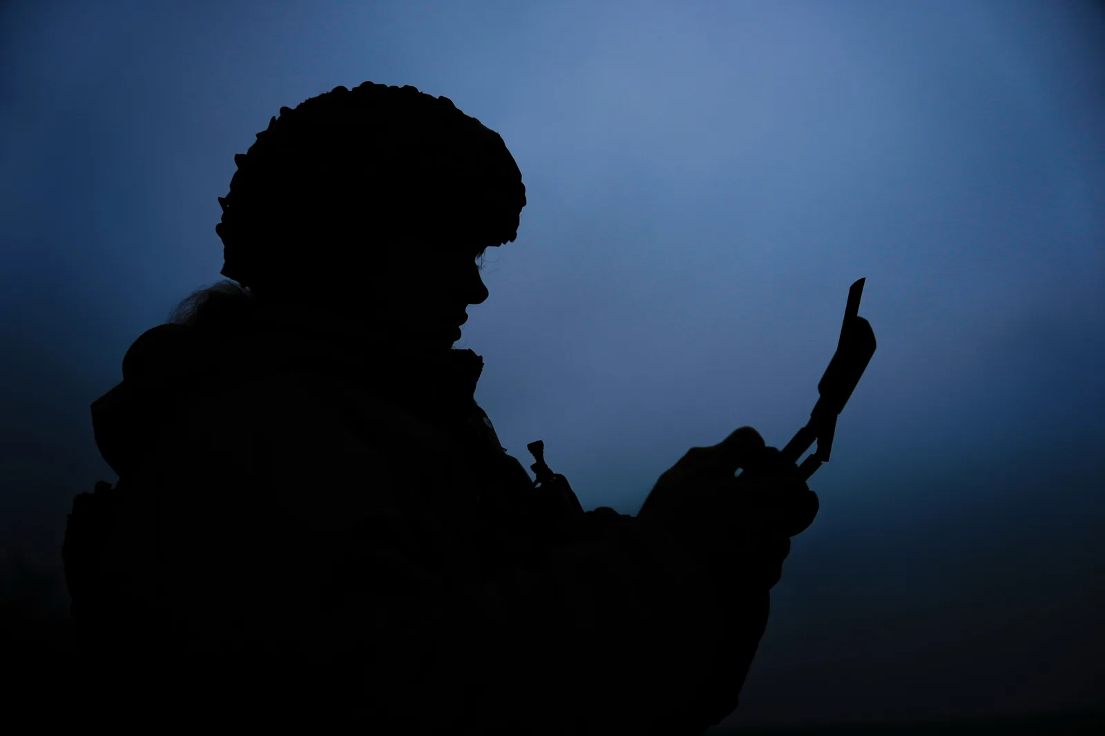 Silhouette a unei persoane care folosește un dispozitiv mobil în întuneric.