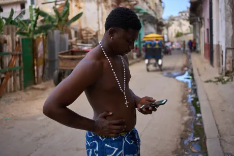 Tânăr pe stradă, verificând telefonul în Cuba, în condiții dificile.