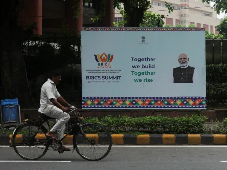 Un bărbat pe bicicletă trece pe lângă un banner al summitului BRICS la New Delhi.