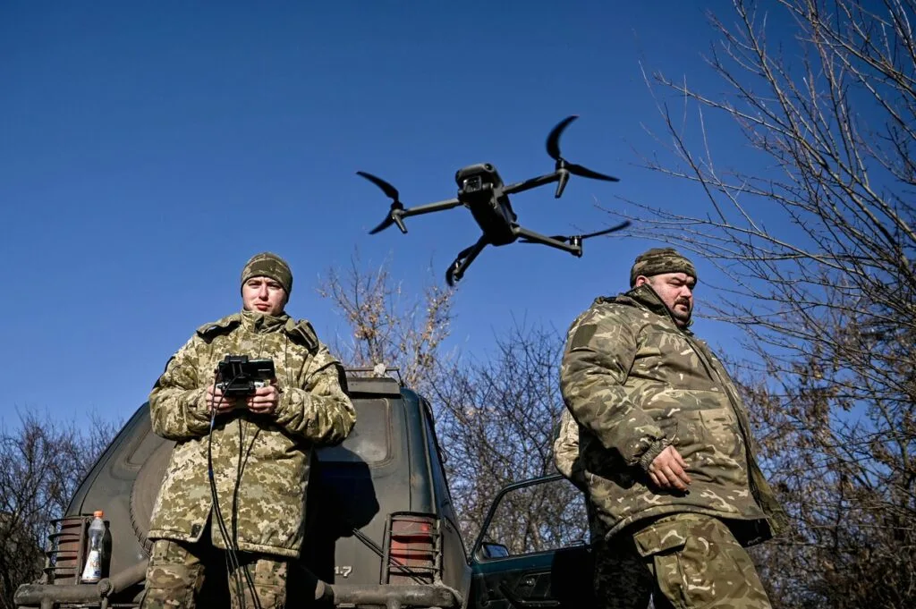 Doi soldați ucraineni operând drone într-un peisaj de război.