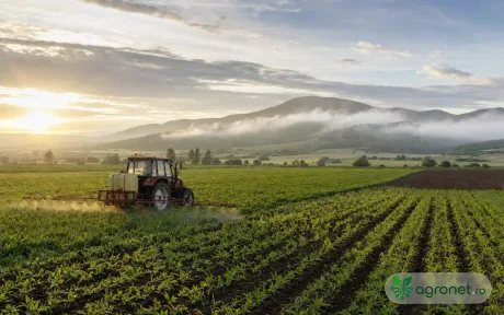 Tractor pe câmp la răsărit, pregătit pentru lucrări agricole.