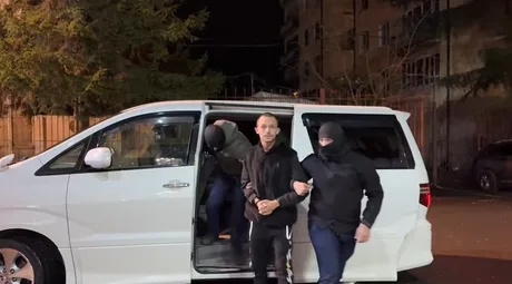 Un bărbat escortat de agenți în fața unei mașini albe, în noapte.
