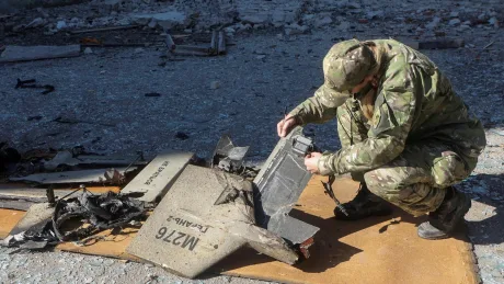 Soldat inspectând resturi de dronă distrusă pe teren.