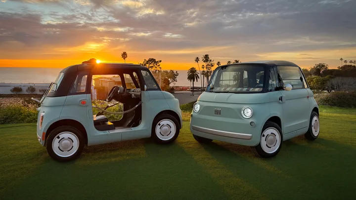 Două microvehicule electrice Fiat Topolino pe un teren verde, cu apus în fundal.