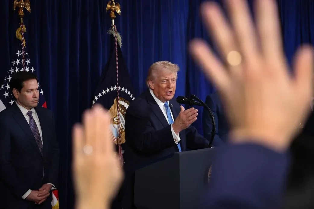 Donald Trump vorbește la un eveniment oficial, cu mâinile ridicate.