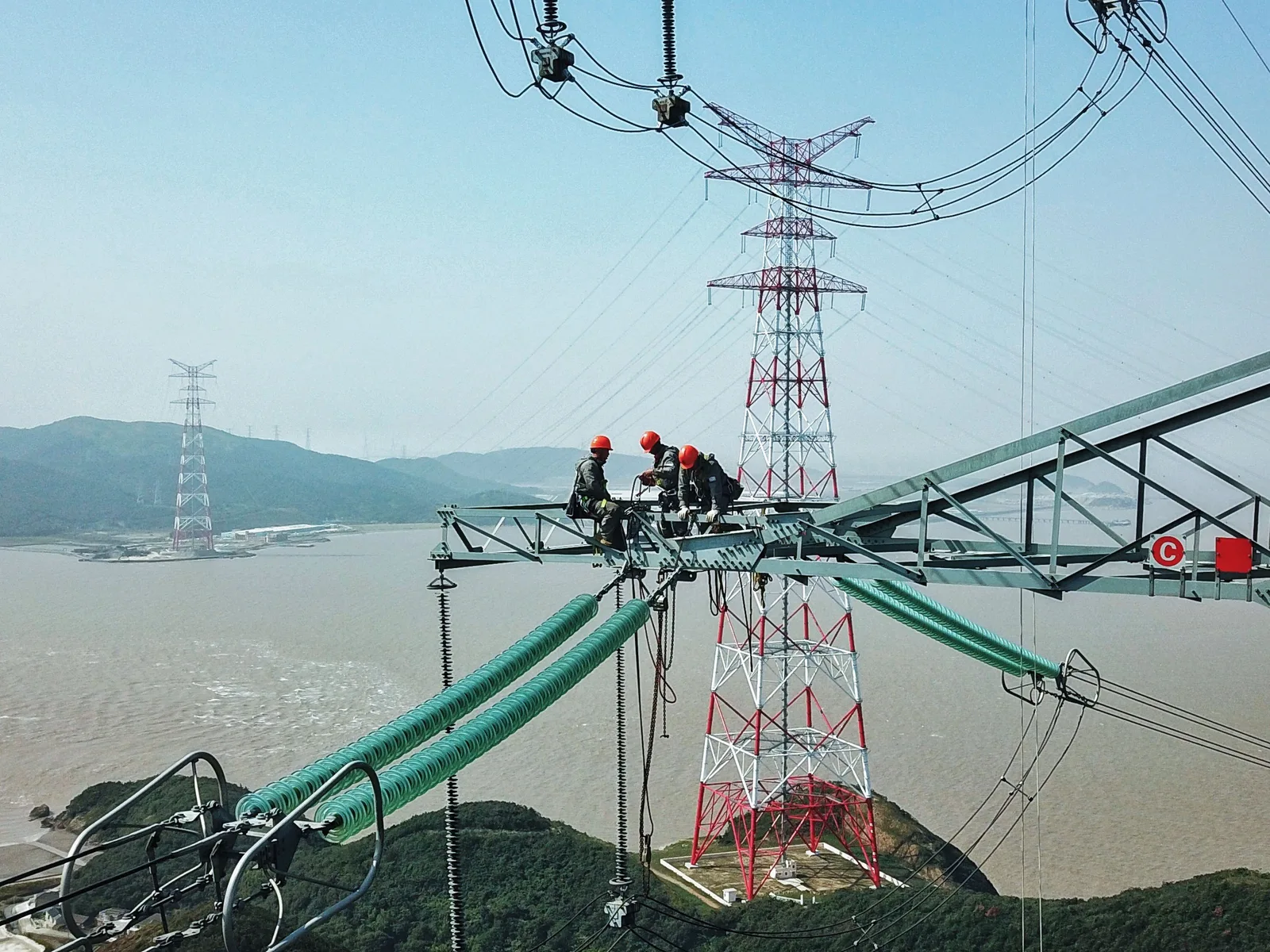 Tehnicieni lucrând la linii electrice în China, evidențiind expansiunea energetică.