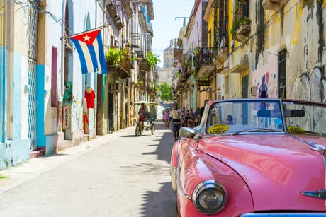 Stradă din Havana cu mașini clasice și steagul Cubei fluturând.