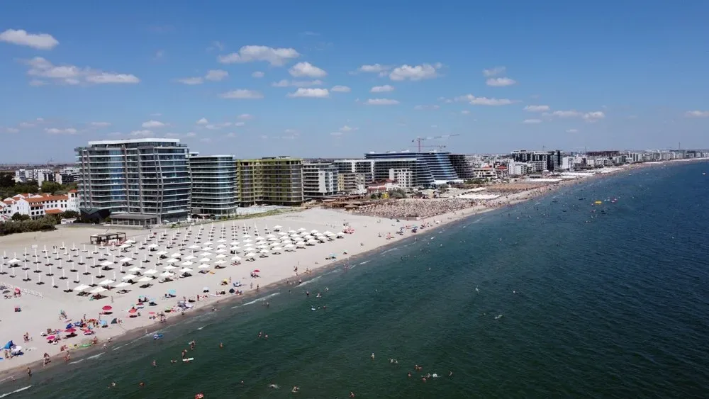 Plajă aglomerată pe litoralul românesc, cu hoteluri moderne.