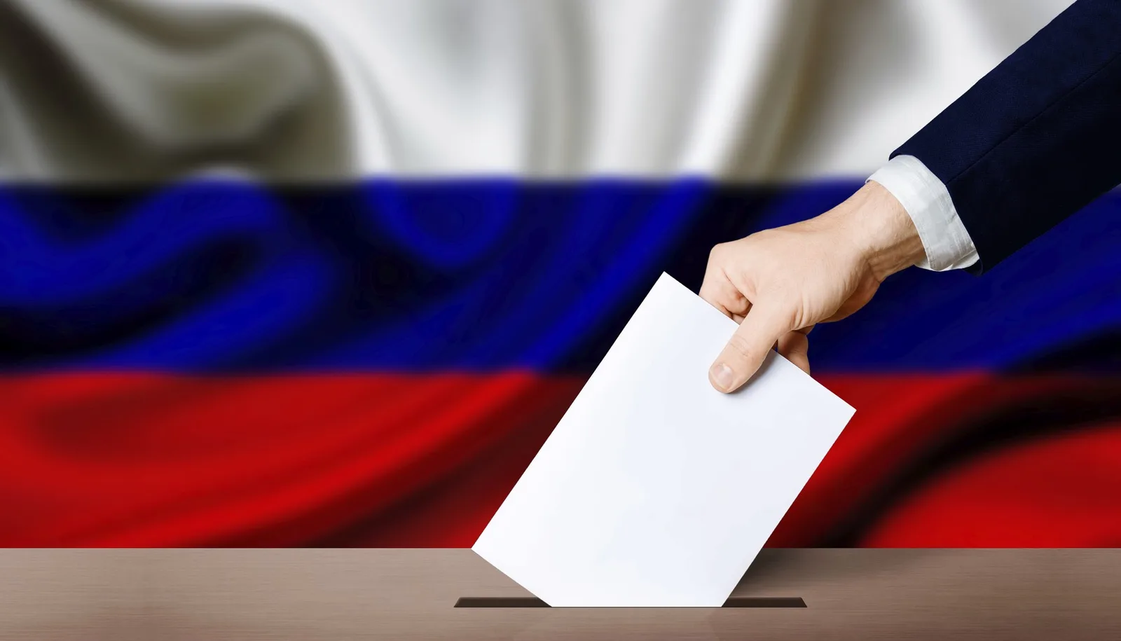 Un alegător depune un buletin de vot în cutia poștală, cu steagul Rusiei în fundal.