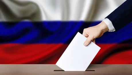 Un alegător depune un buletin de vot în cutia poștală, cu steagul Rusiei în fundal.