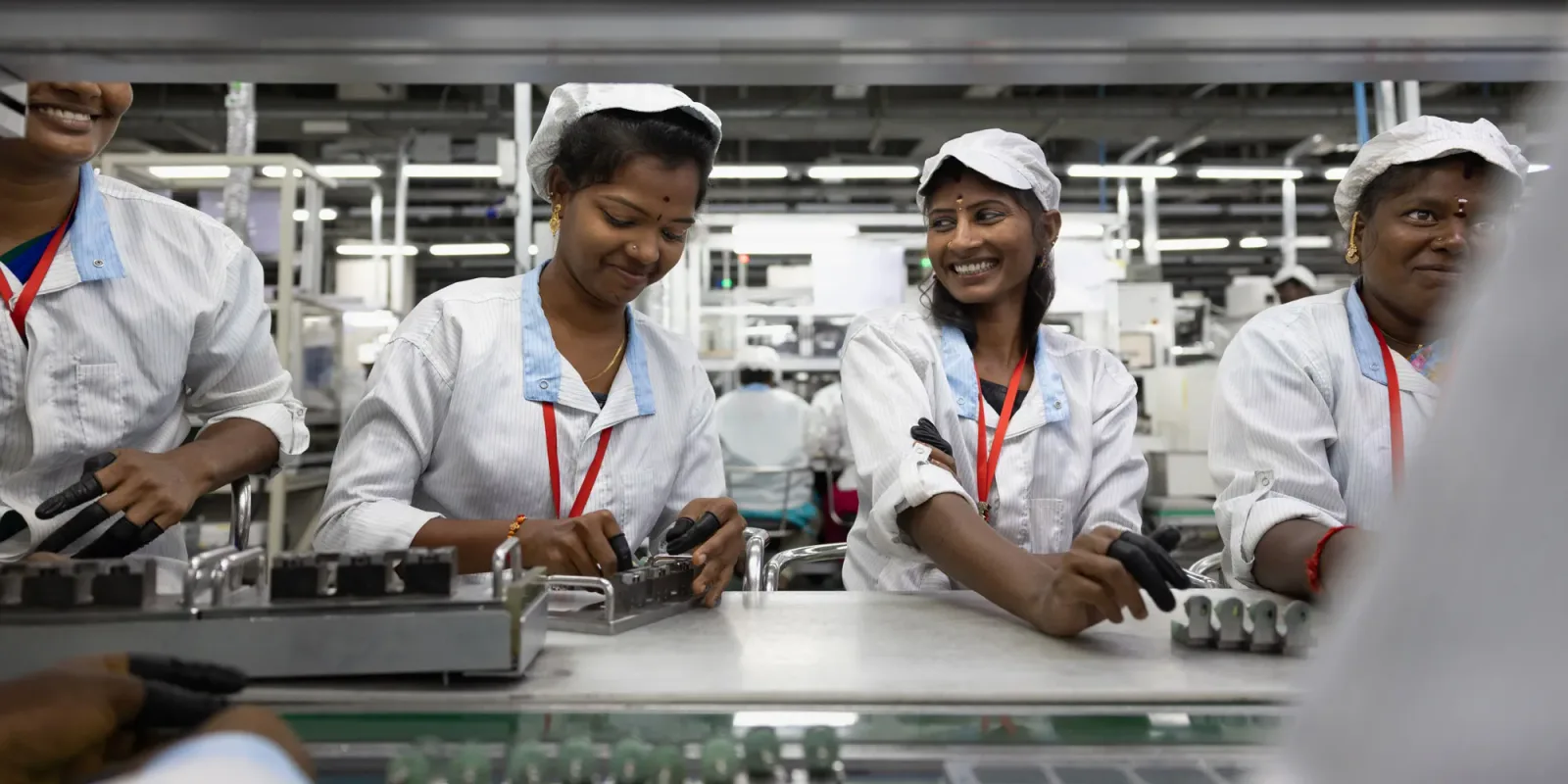 Angajați la o fabrică de componente electronice din India, zâmbind în timpul lucrului.