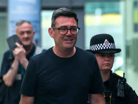 Andy Burnham zâmbind în timp ce este însoțit de poliție.